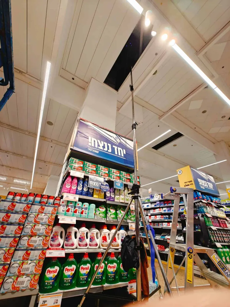 סורק על חצובה גבוהה בין מדפי החנות, מתחת לפתח בתקרה