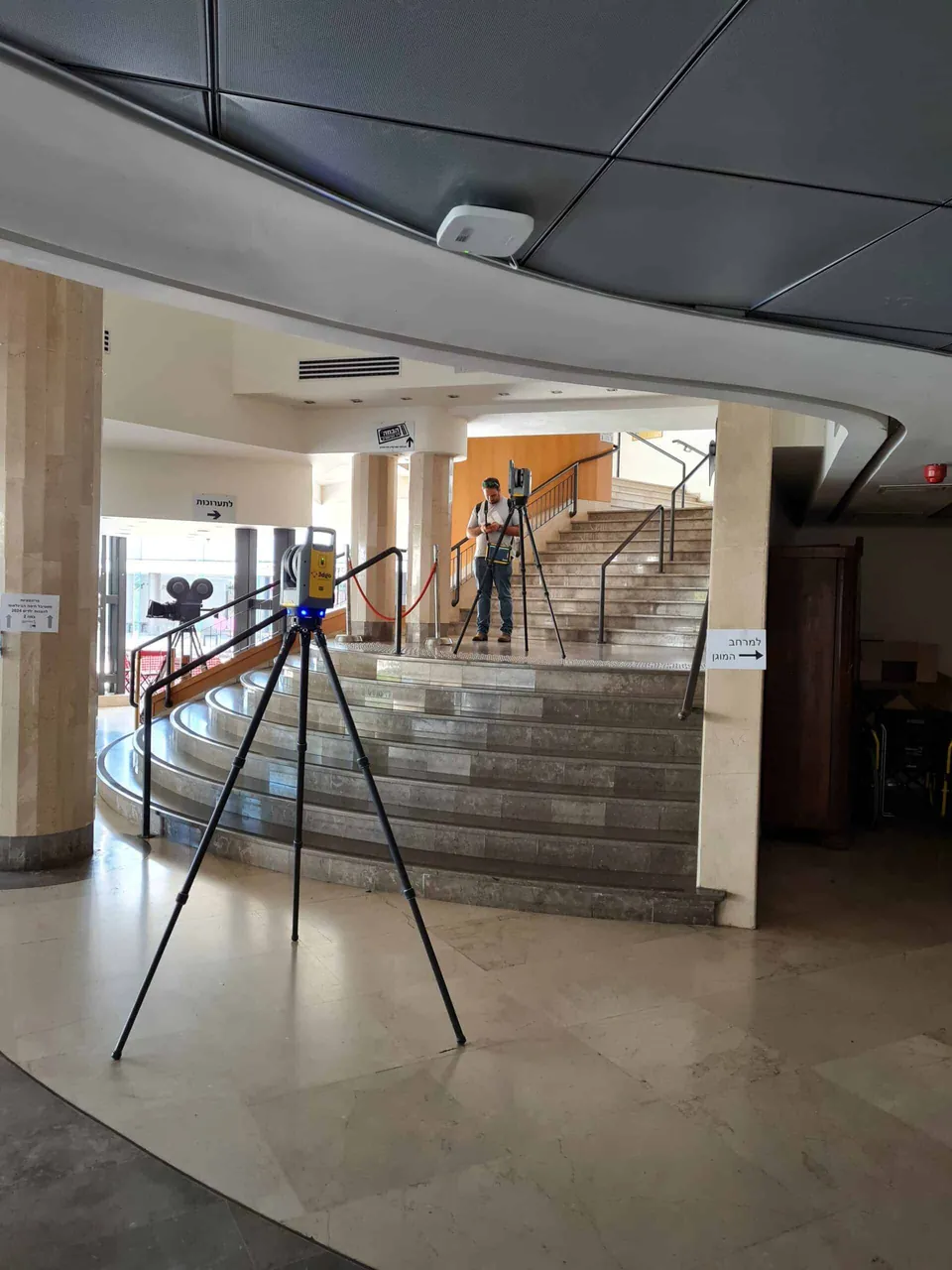 סורק לייזר על חצובה בלובי ליד גרם מדרגות רחב, ומודד ברקע